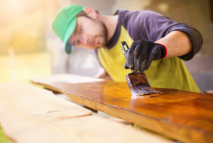 Handyman varnishing wooden planks outside